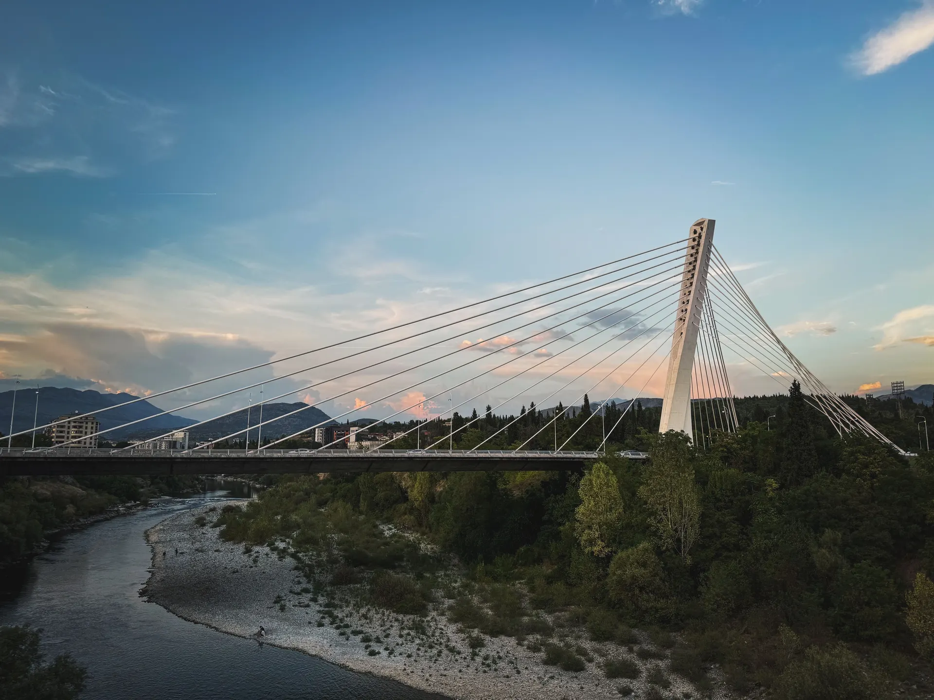 Un ponte strallato attraversa la valle di un fiume alla luce della sera: il pilone in calcestruzzo regge il ventaglio dei cavi sopra l'impalcato