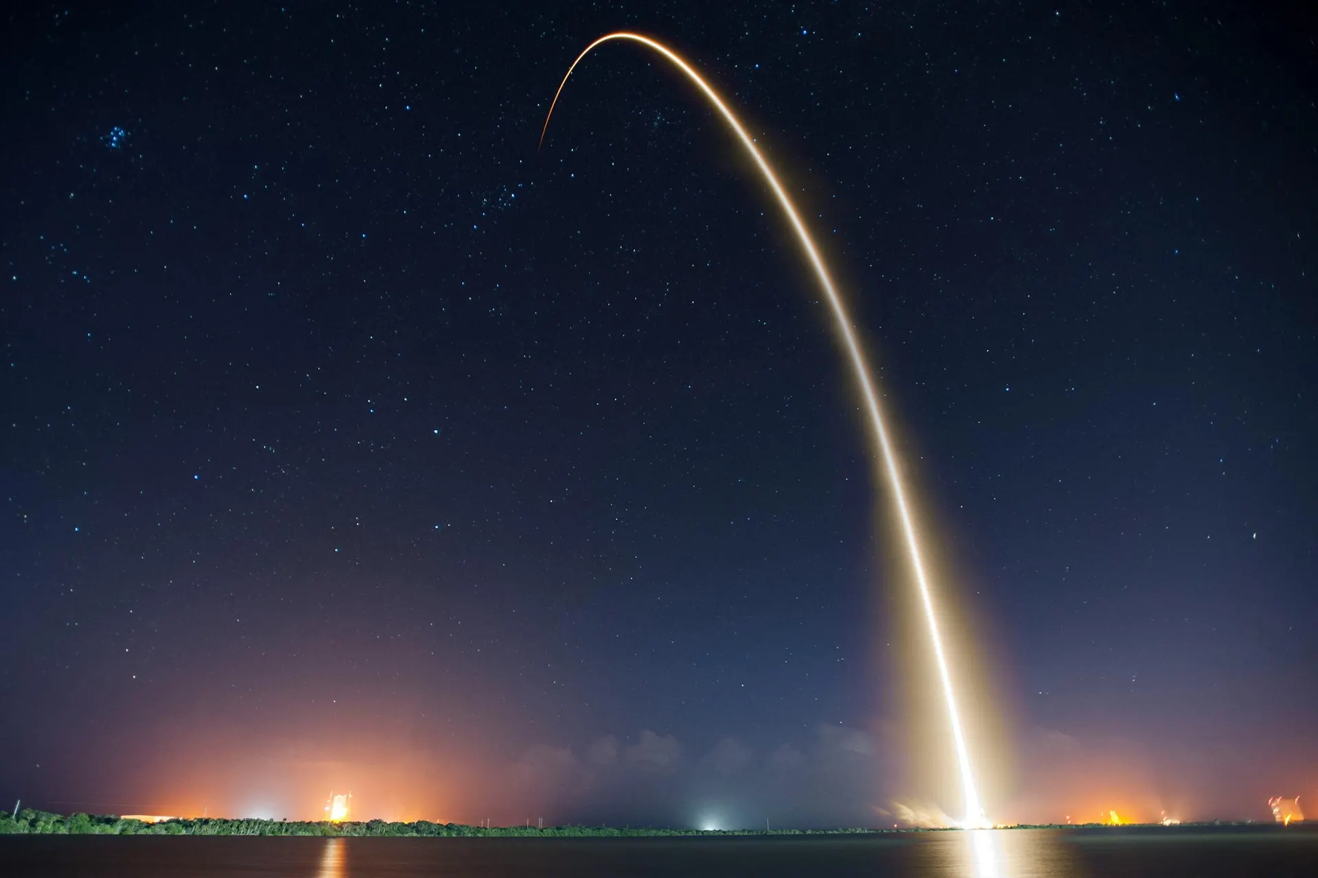 La scia luminosa di un lancio spaziale che curva nel cielo stellato sopra il mare