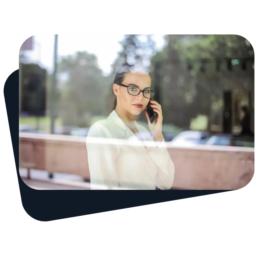 Una donna con gli occhiali parla al telefono, ripresa attraverso la vetrata di un ufficio