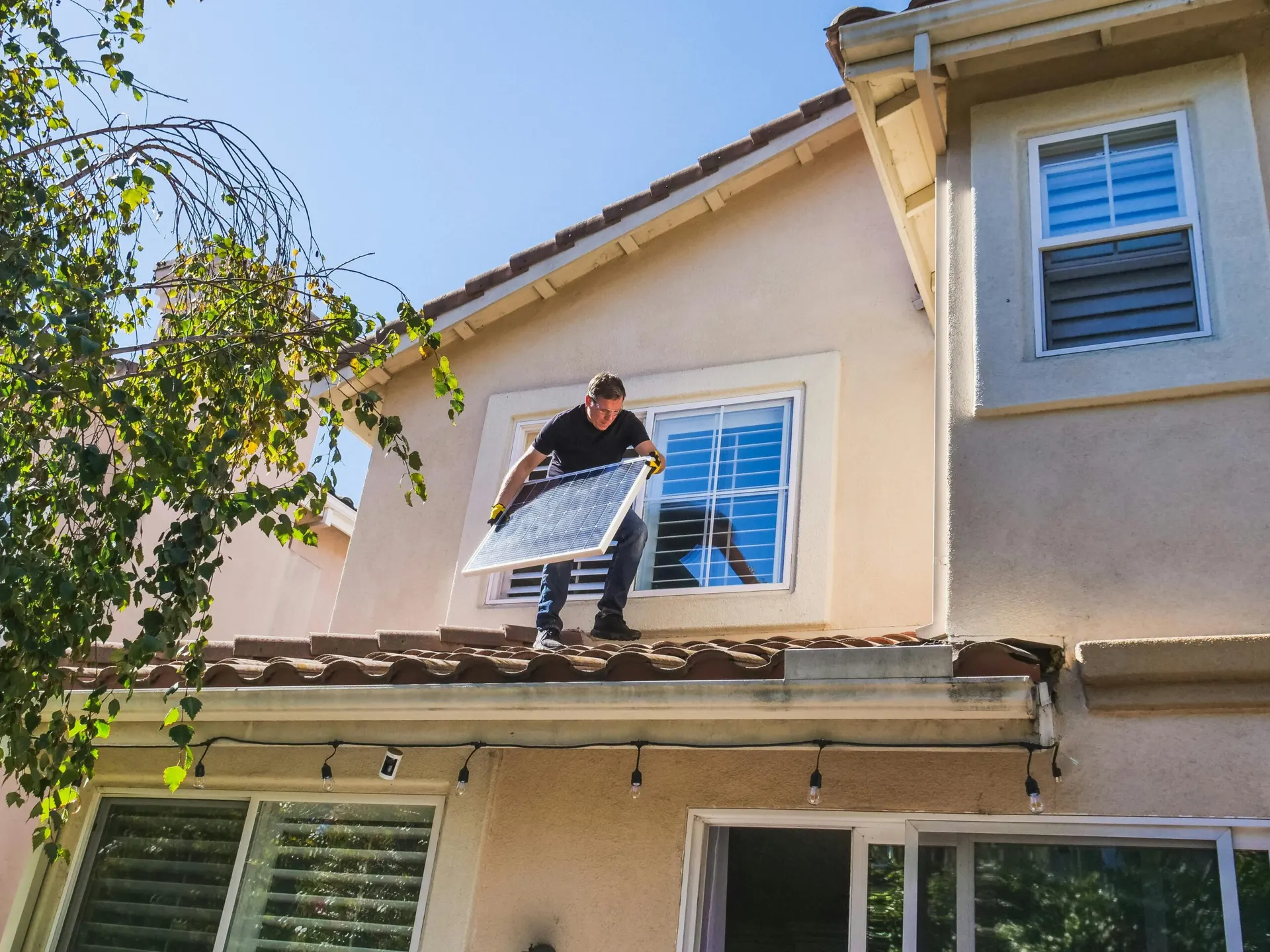 Un uomo in piedi sul tetto di una casa regge un pannello fotovoltaico